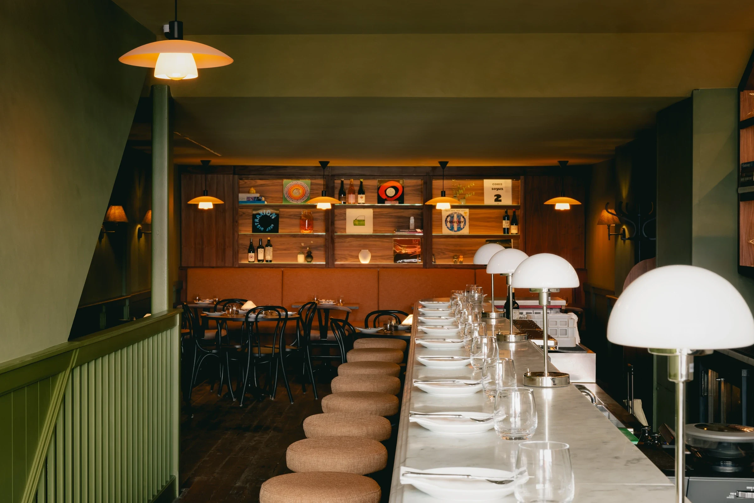 The counter at sova running into the dining room, dome lamps lit against olive walls.