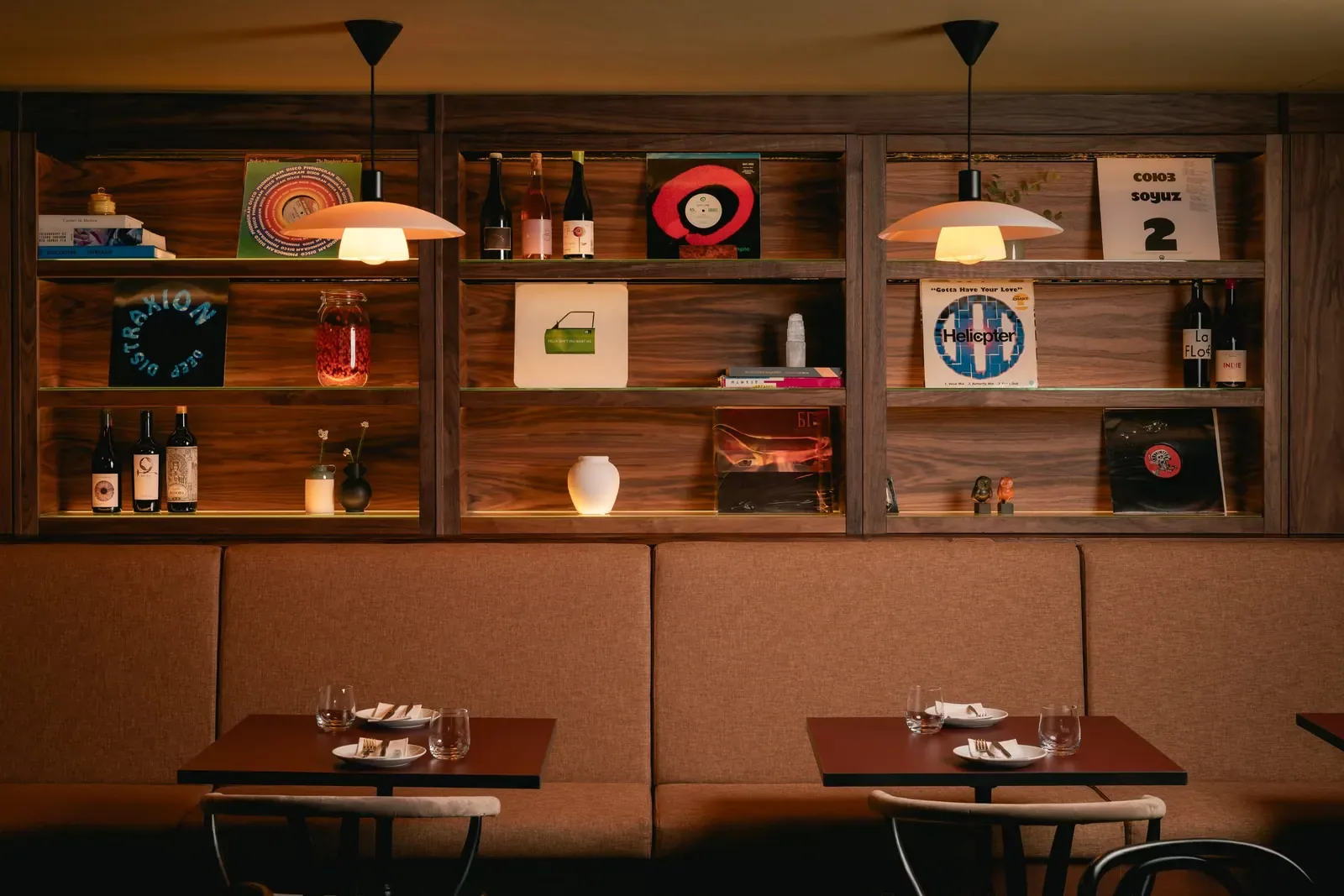 Banquette seating beneath walnut shelves of records, wine bottles and ceramics.
